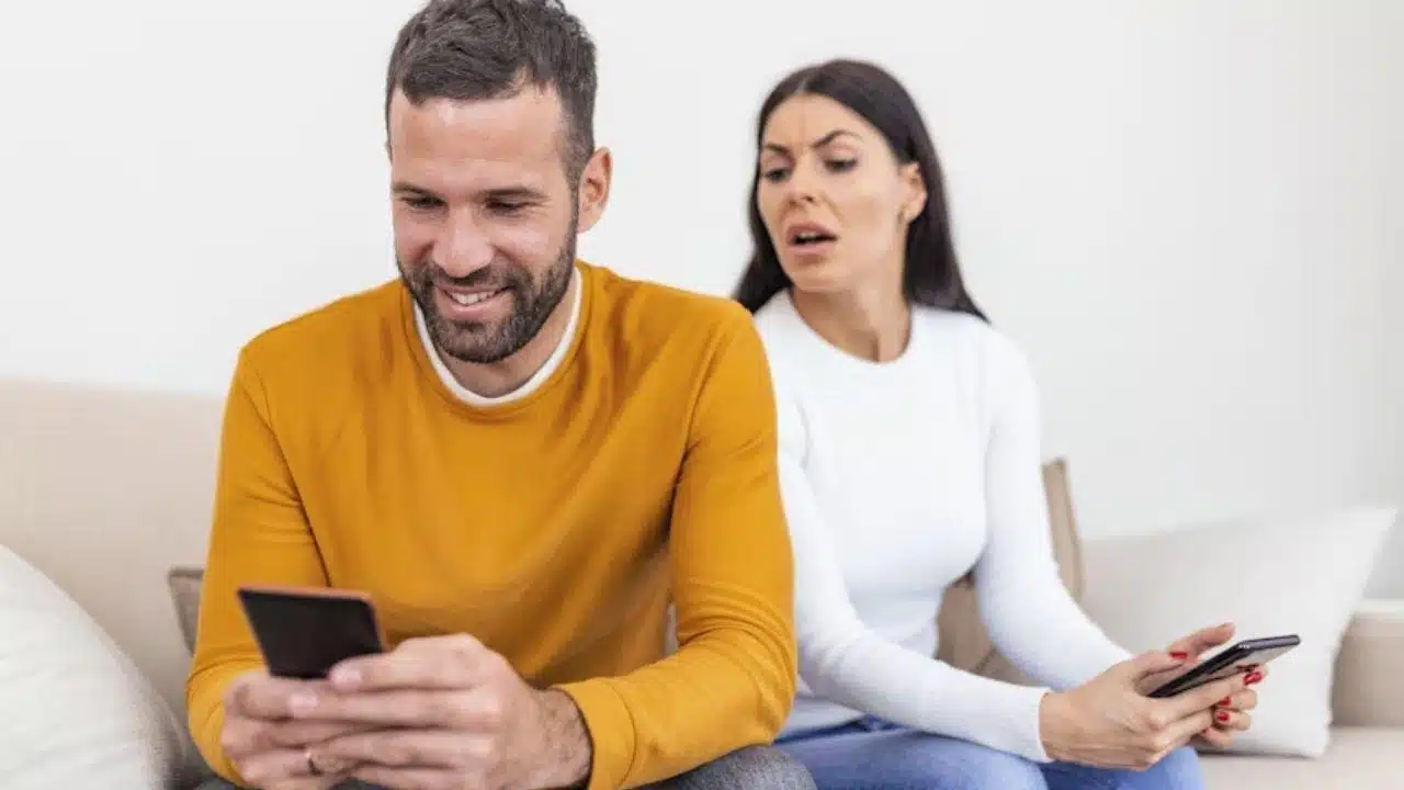 A man scrolling through social media while his wife looks at him with concern.