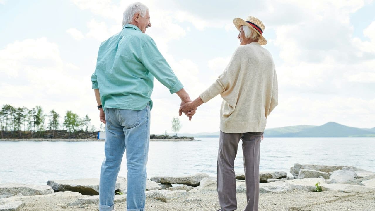 A senior couple holding hands and looking at each other by the water.