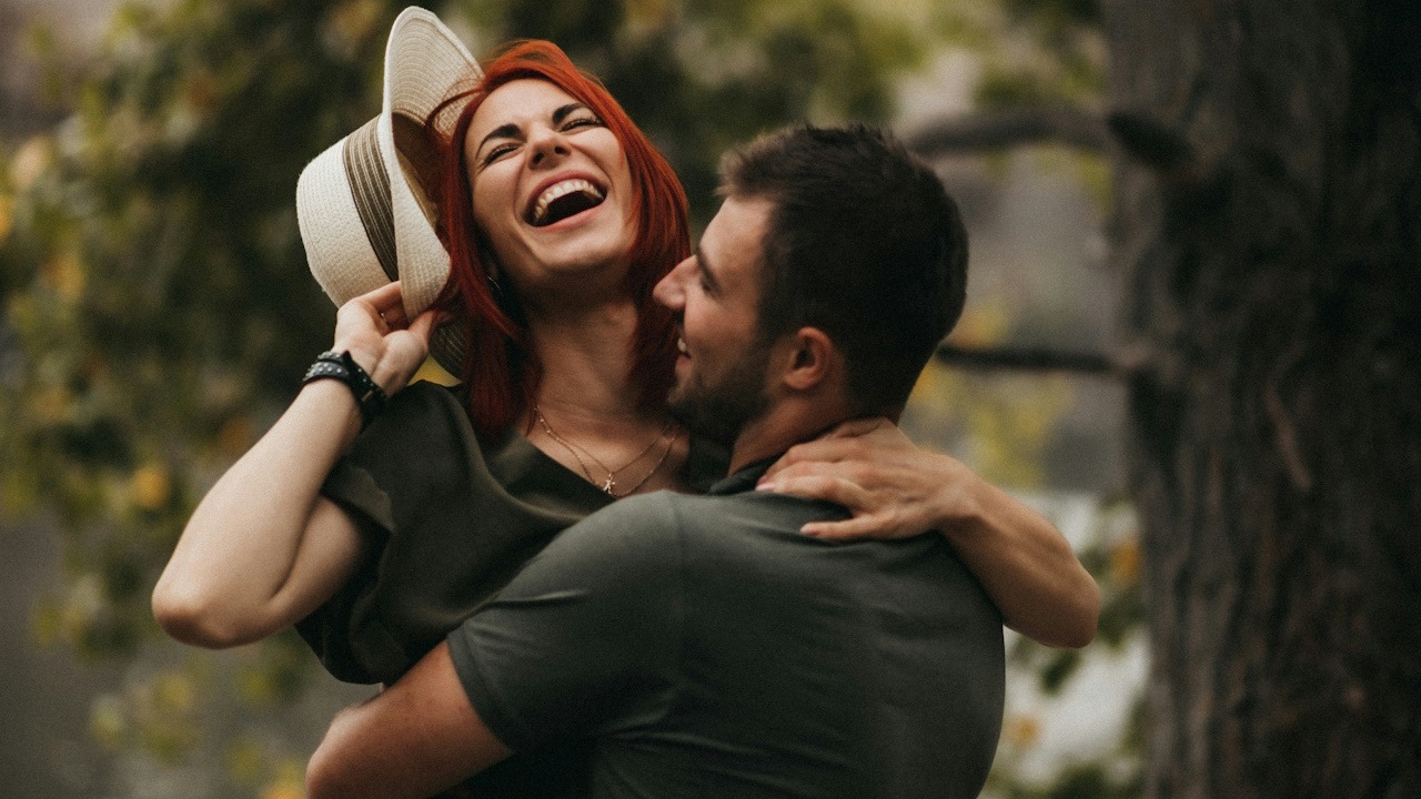 A man holding up his wife who’s holding a hat in one hand