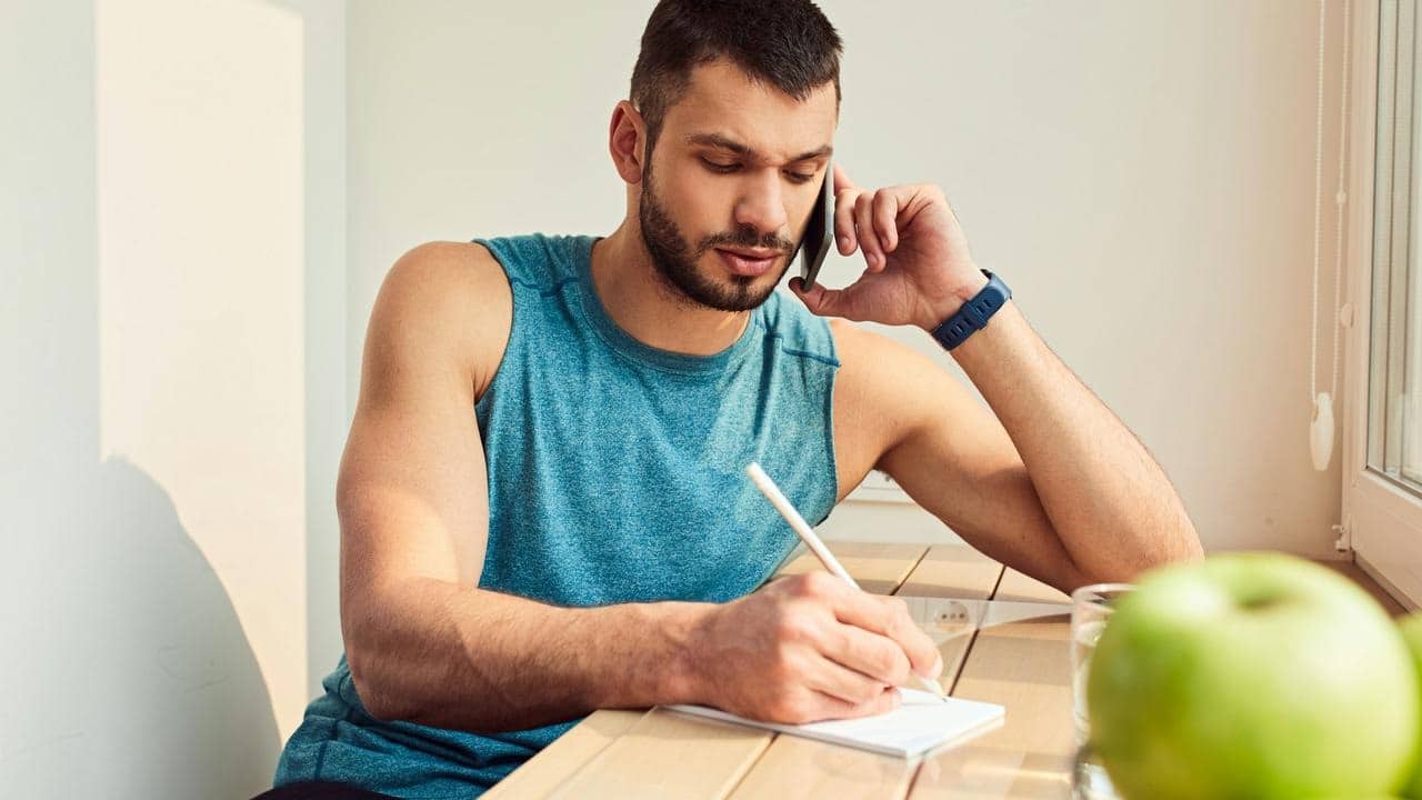 A man on a phone call writing notes at a table.