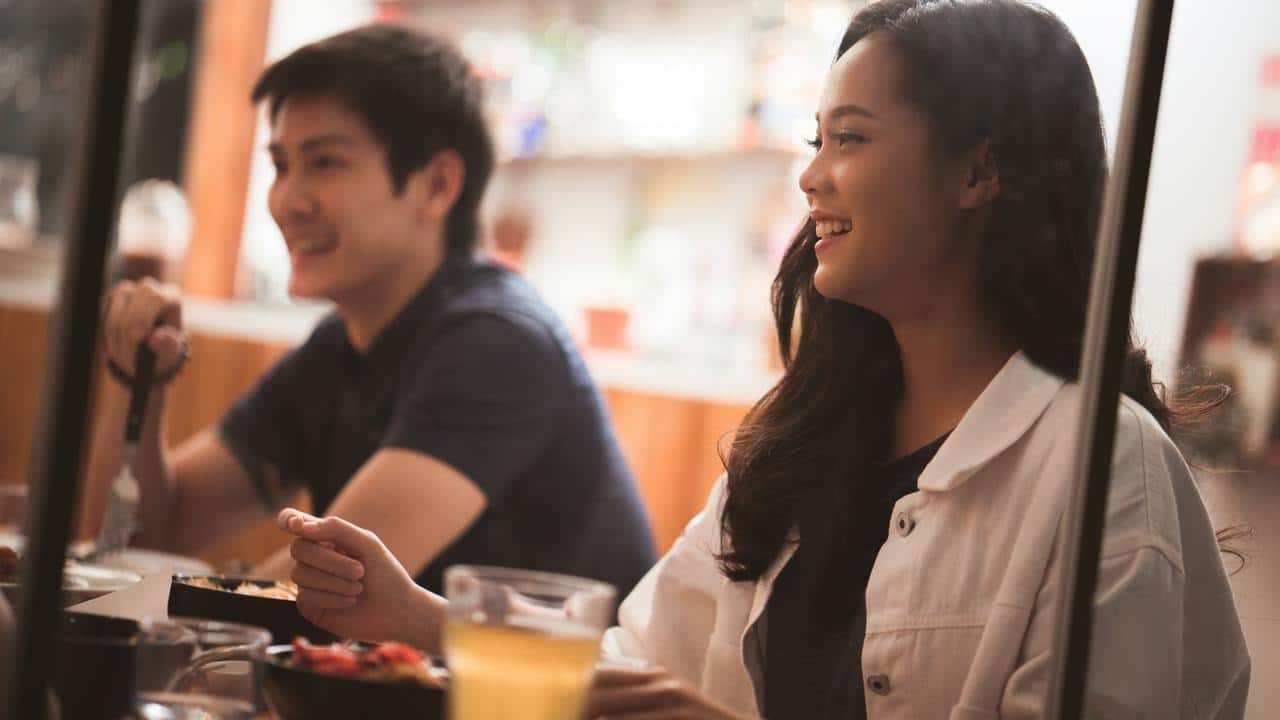 A woman smiling at a restaurant table with a dining companion.