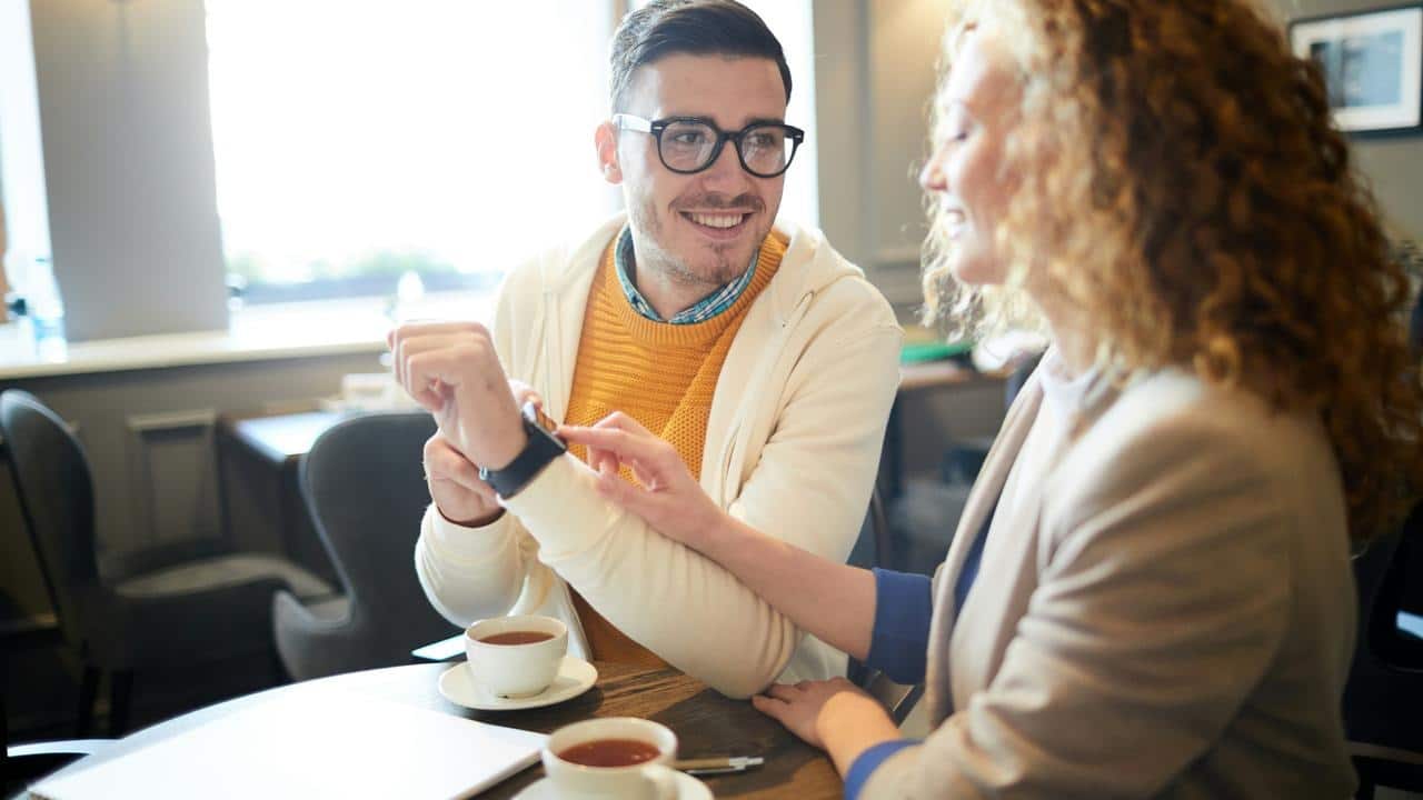 A man and a woman looking at a smartwatch over coffee.
