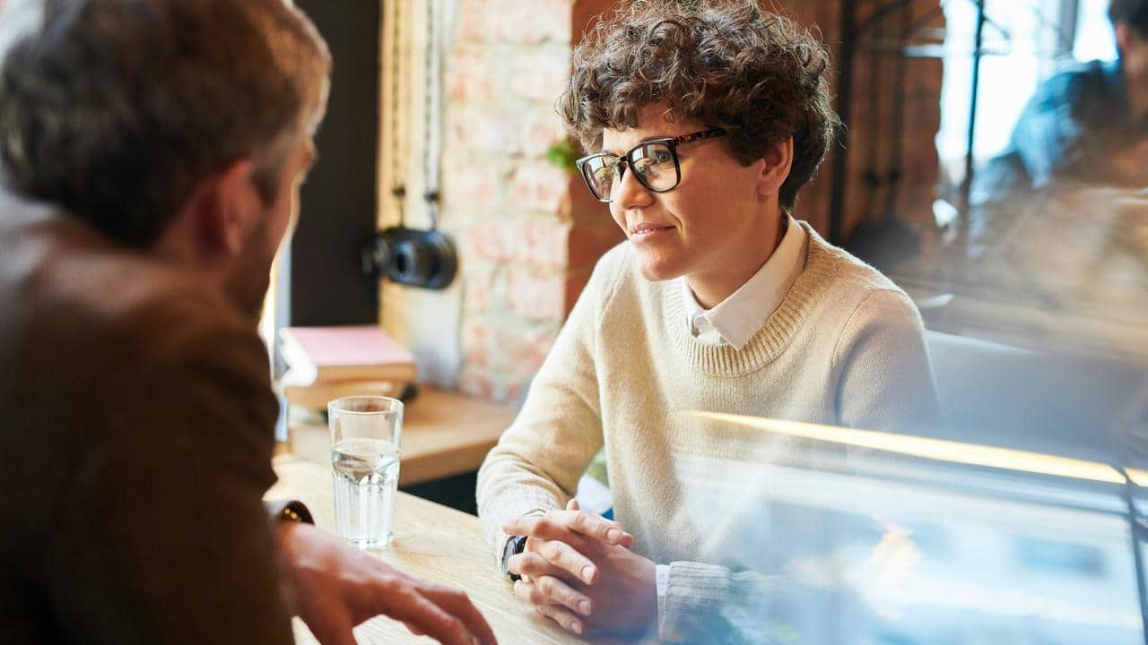A person with curly hair and glasses listening at a table.