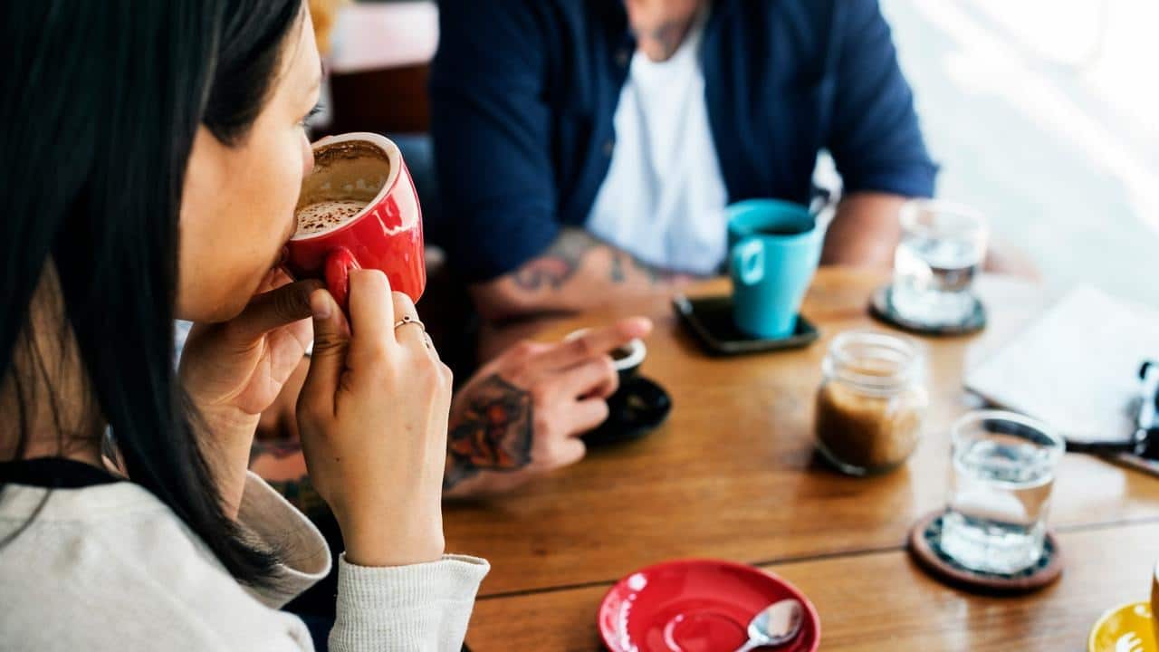 A woman sipping coffee at a table with a companion.