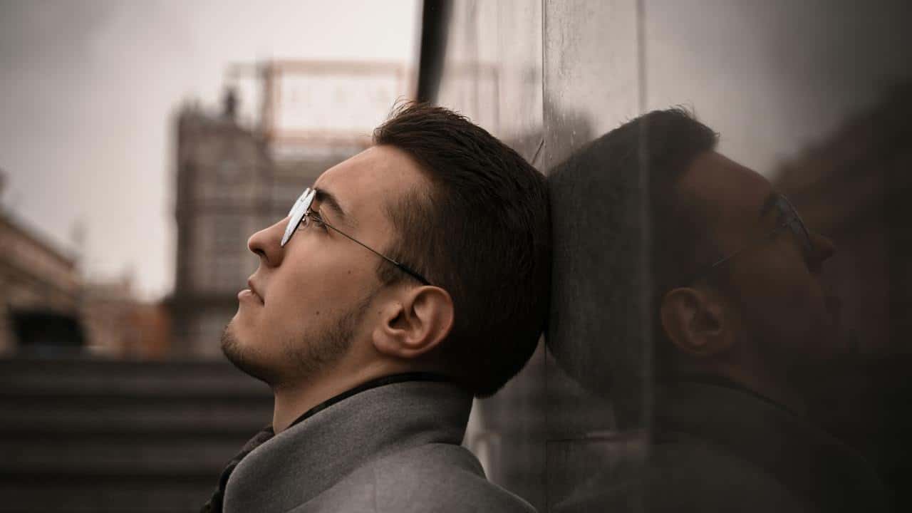 A man leaning against a reflective wall looking upward.