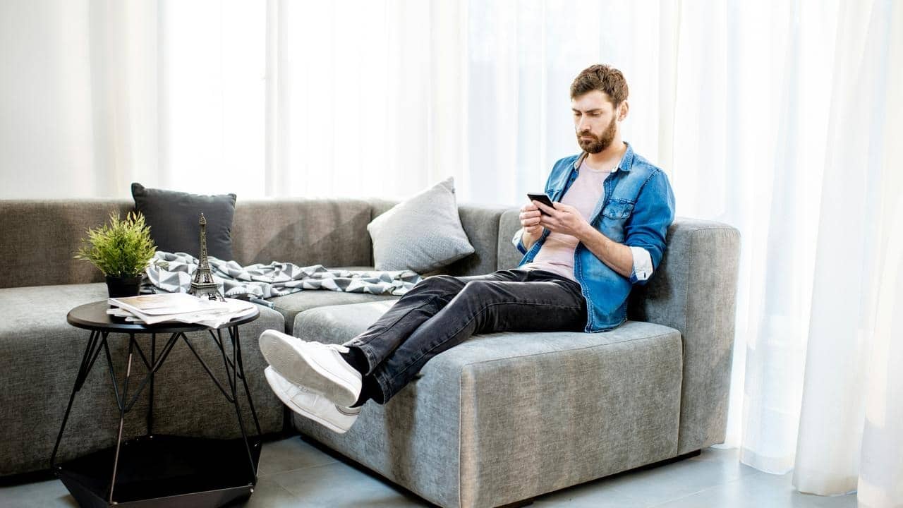 A man sitting on a sofa checking his phone.