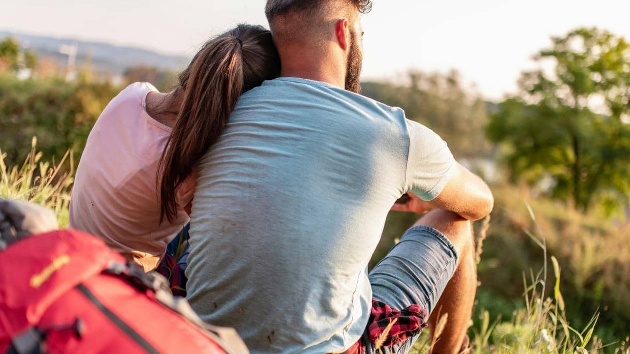 A couple sitting on a hillside with a backpack.