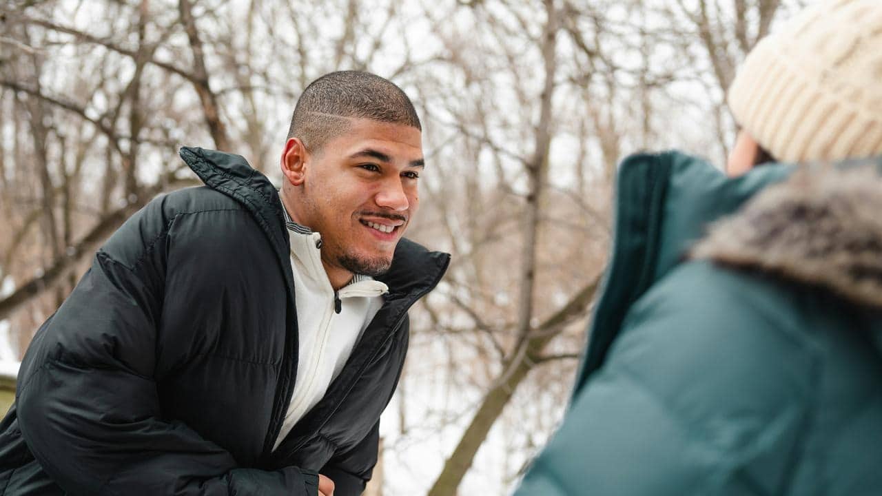 A man in a puffy winter jacket smiling outdoors.