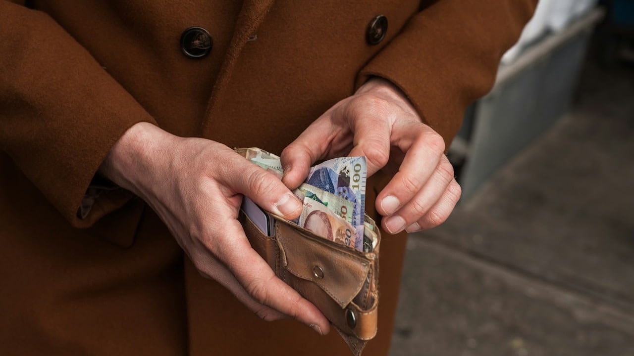 A person in a brown coat is holding a wallet full of money.