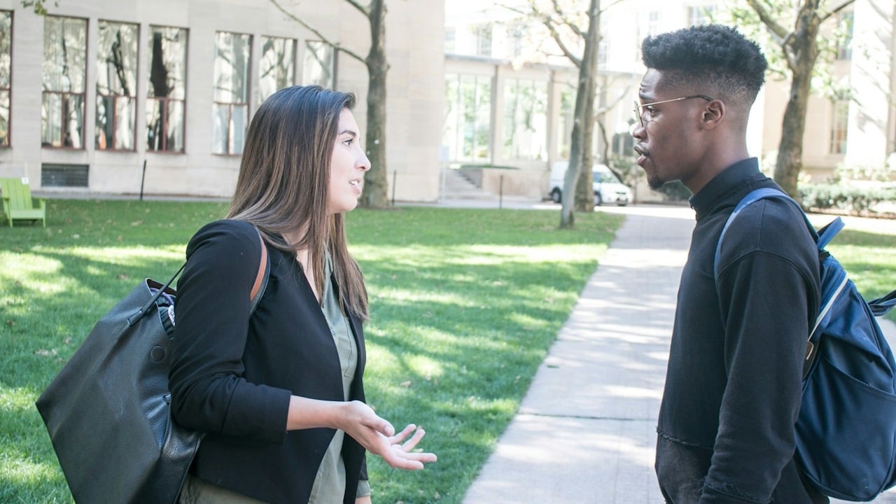 A woman gesturing at a man while they stand outside.