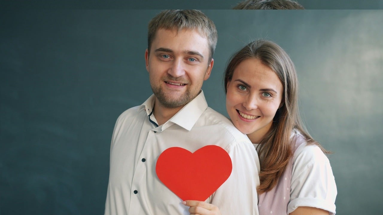 A happy mature couple hugging outdoors on a pier by the sea at dusk, looking at each other.