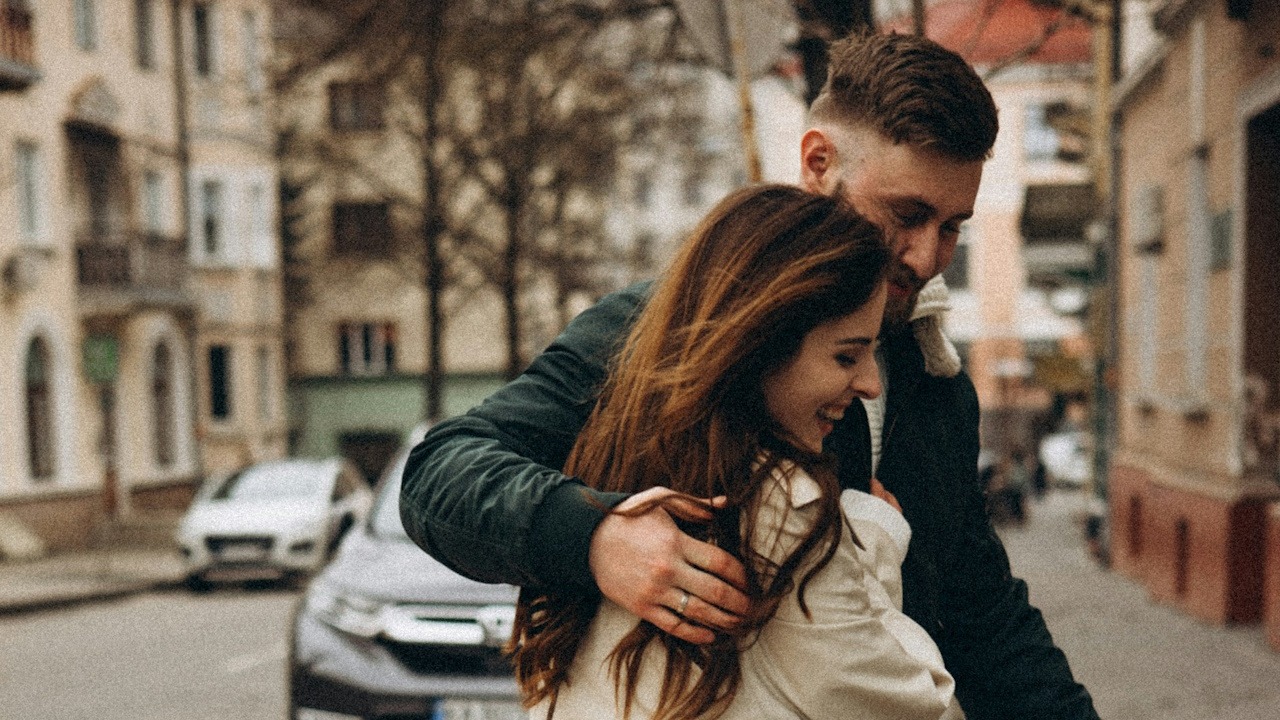 A smiling couple holding each other while walking down a street.