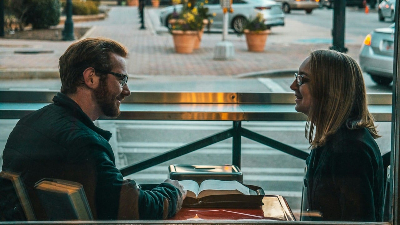 A bespectacled couple smiling and talking with each other in a restaurant.