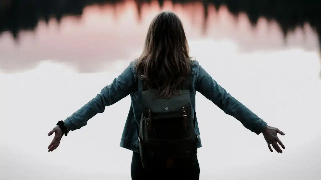 A woman standing while facing a body of water.