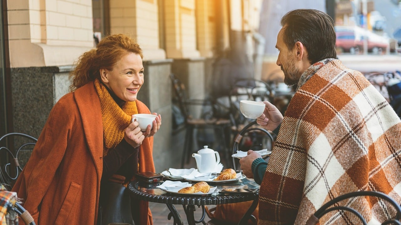 A couple drinking tea and talking in a cafe outdoors.