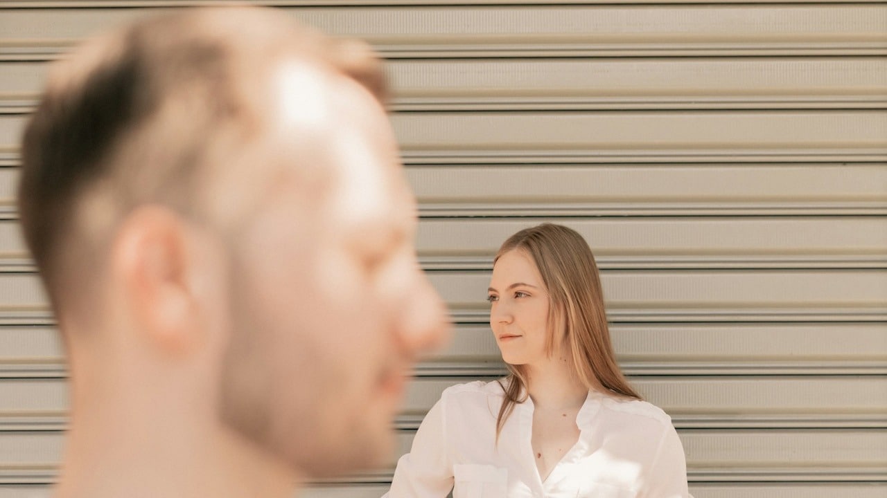 A couple standing outdoors are looking away from each other.