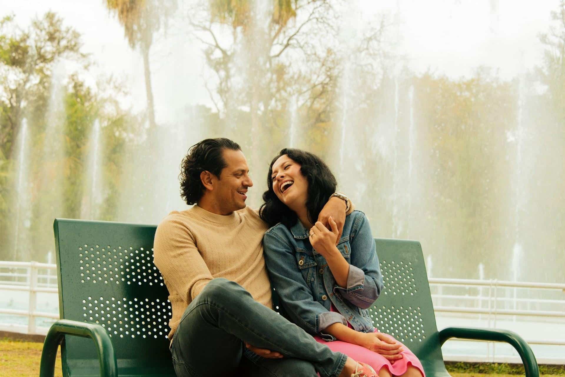 A couple laughing happily while sitting on a bench outdoors.
