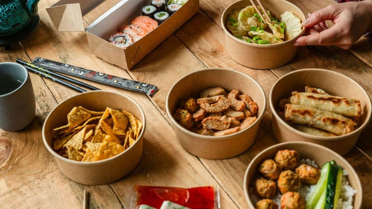 A person picks up a dumpling from a table laden with takeout food.