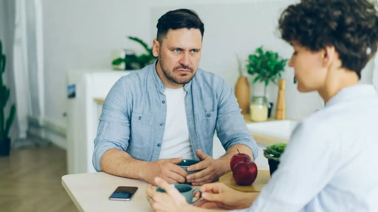 A man with a serious expression listens intently to a woman.