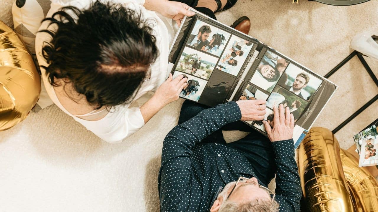 A couple sits on the floor, looking at a photo album together.