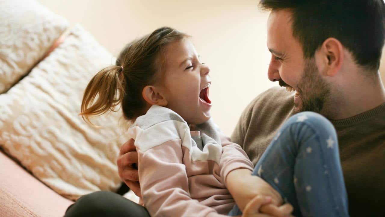 A father and daughter laughing together on a couch.
