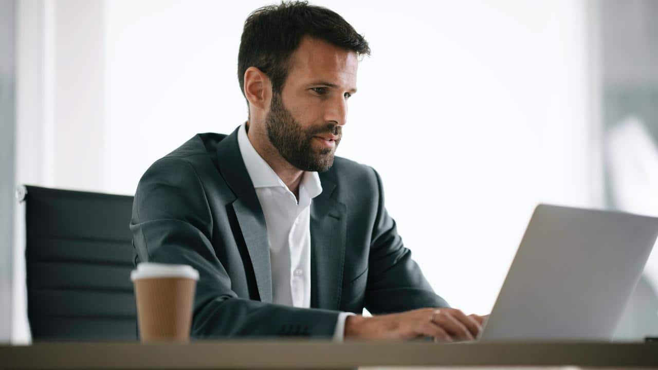 A businessman working on a laptop with a coffee cup nearby.