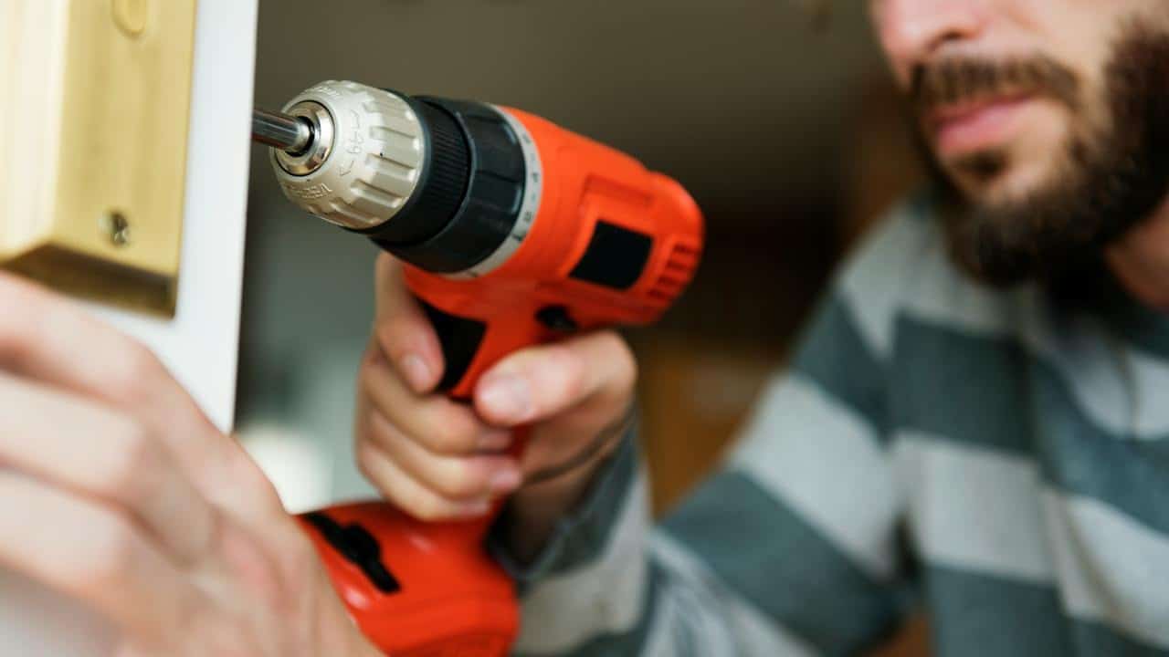 A man using a power drill to fix a door lock.