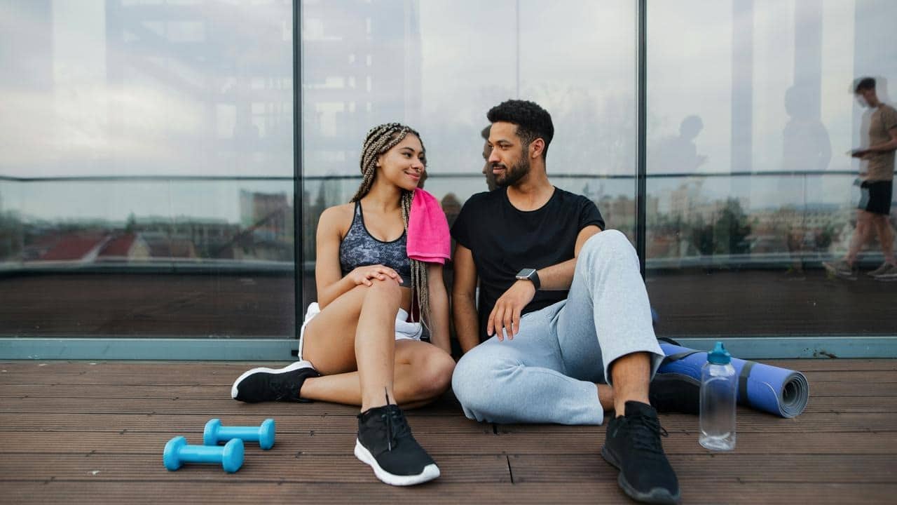 A fit couple sitting and smiling after a workout.