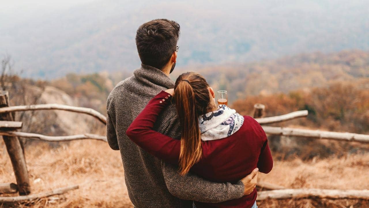 A couple embracing while looking out over a scenic autumn landscape.
