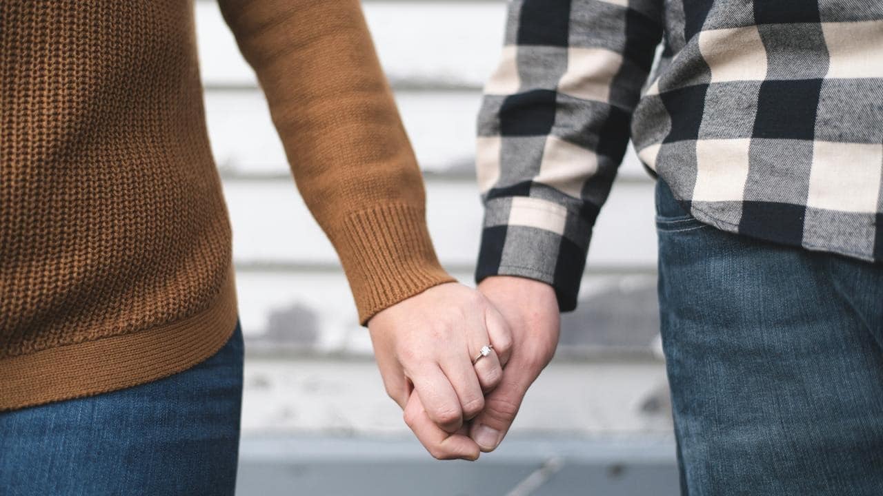A couple holding hands with an engagement ring visible.
