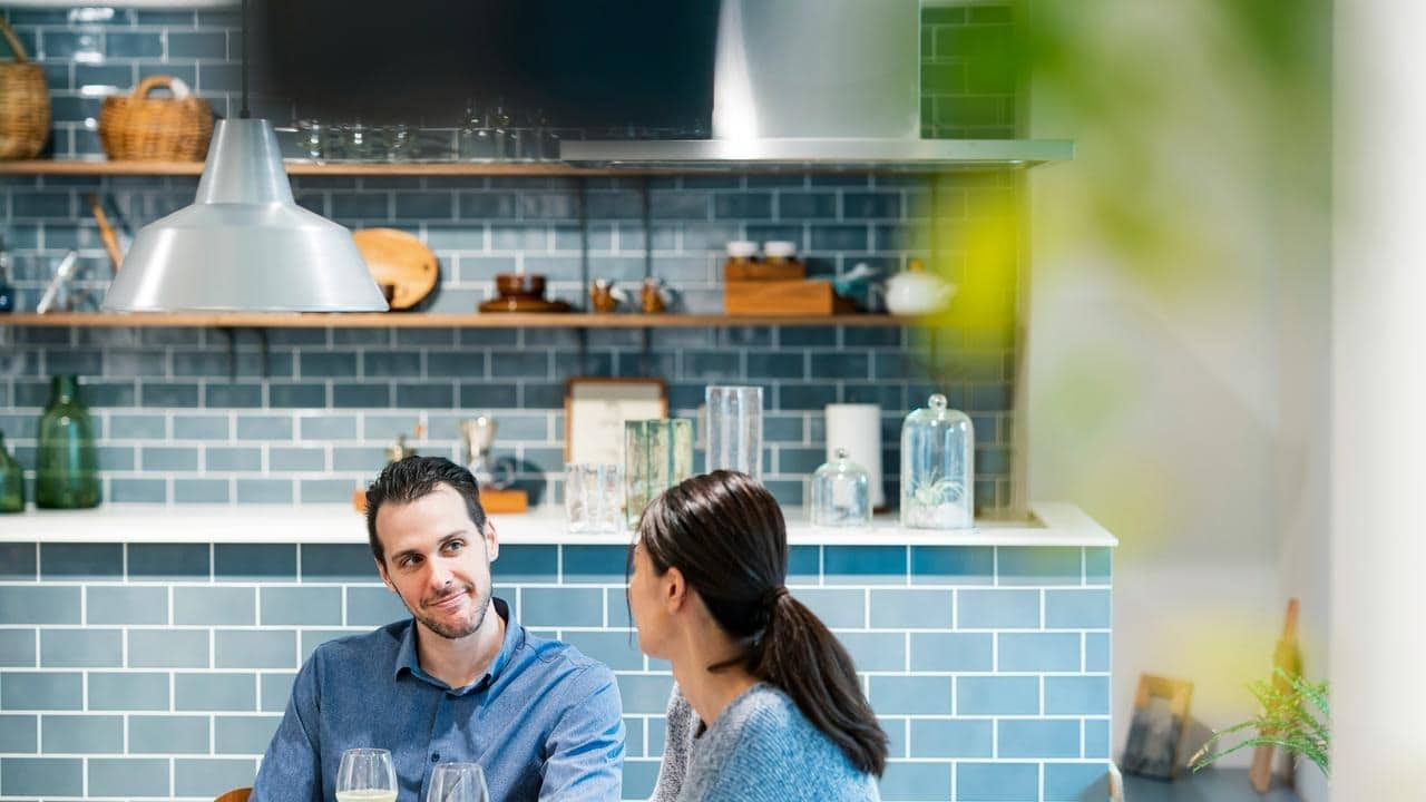 A couple chatting over drinks in a modern kitchen.