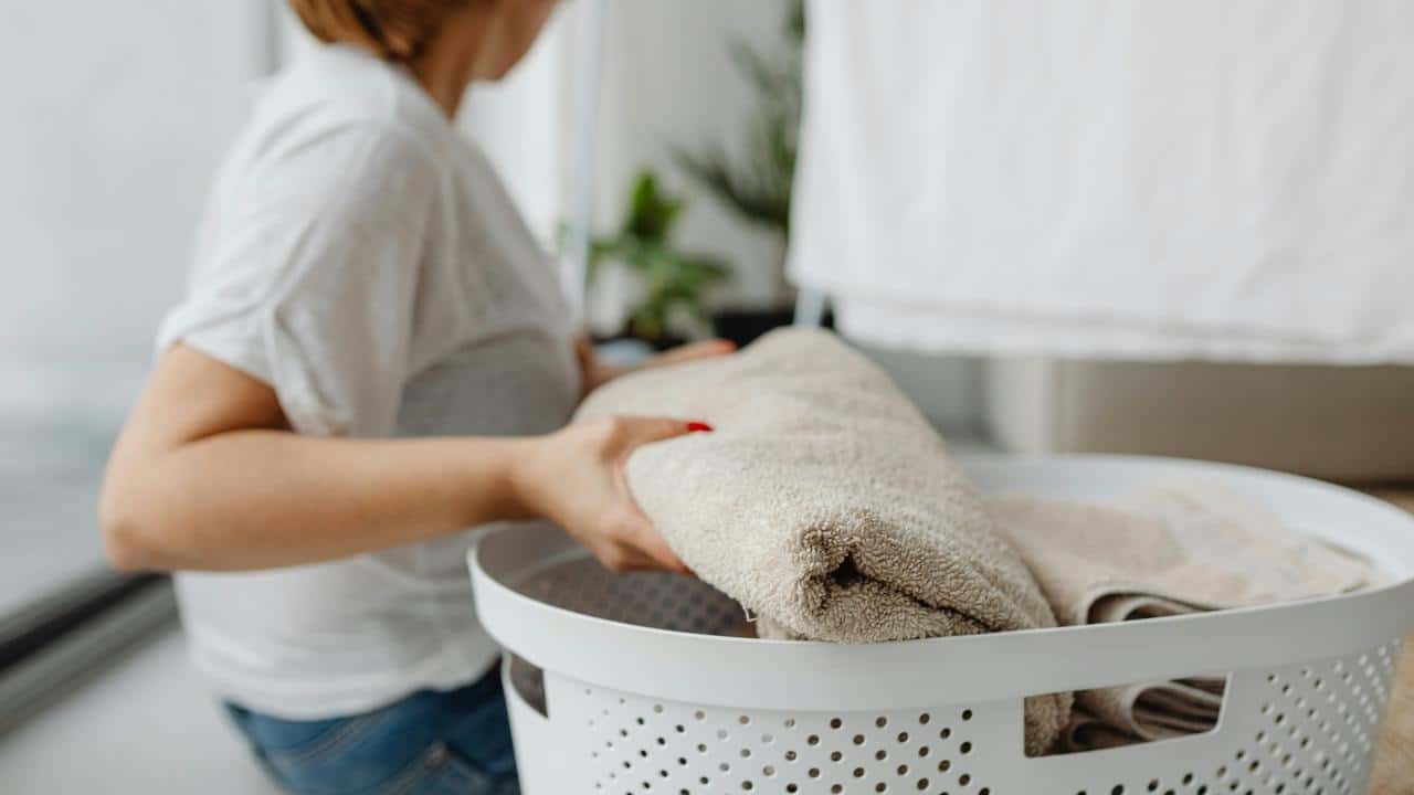 A person placing folded towels into a laundry basket.