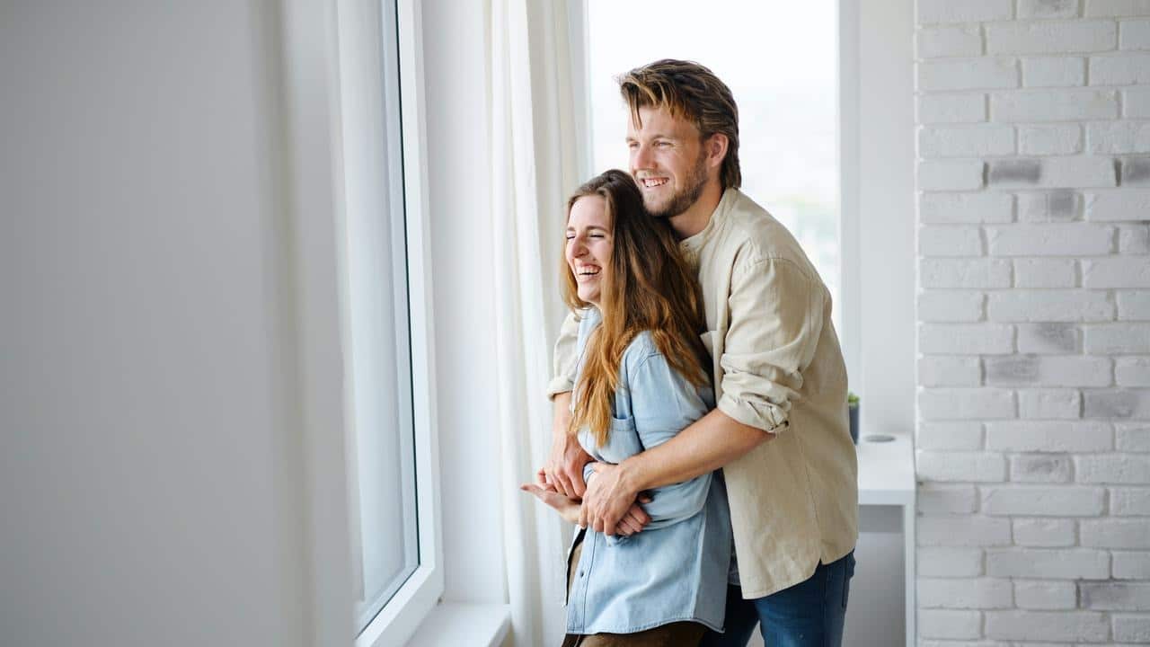 A couple embracing and smiling by a window.