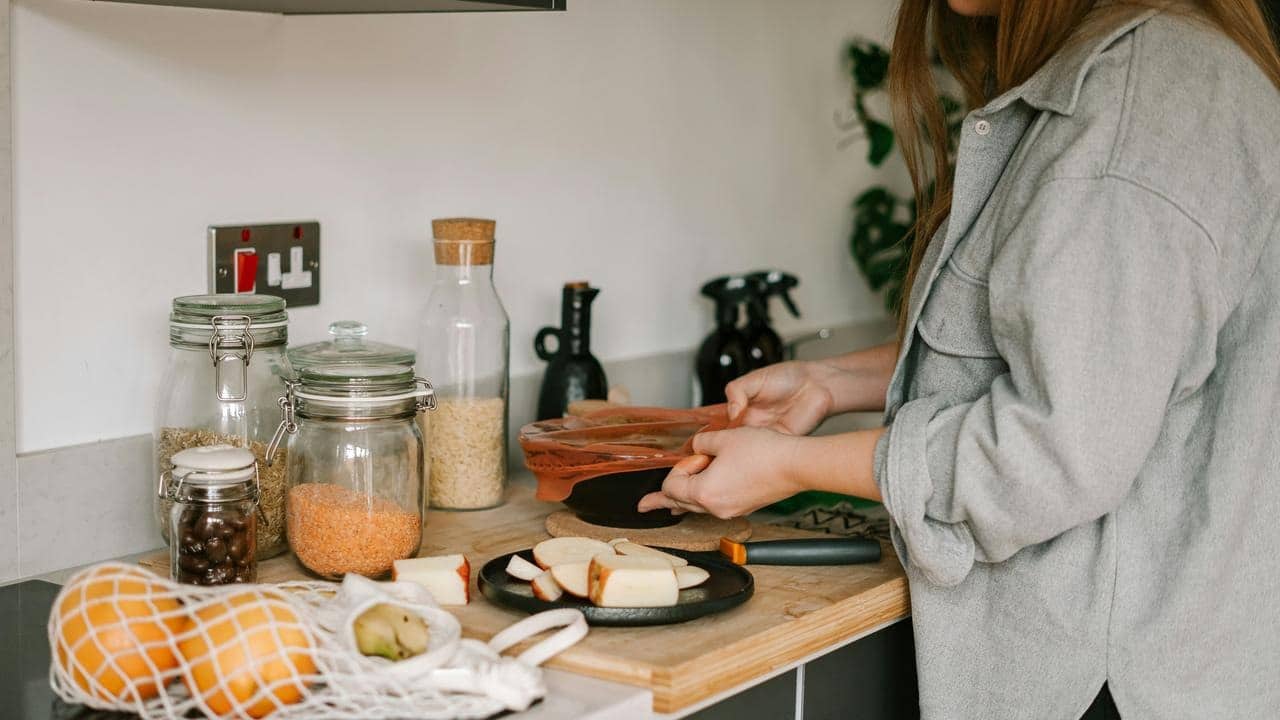 A person arranging sliced fruit and cheese on a kitchen counter.