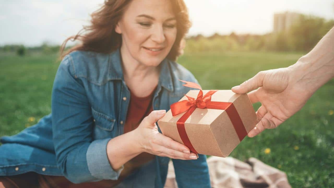 A woman outdoors accepting a ribbon-tied gift box.