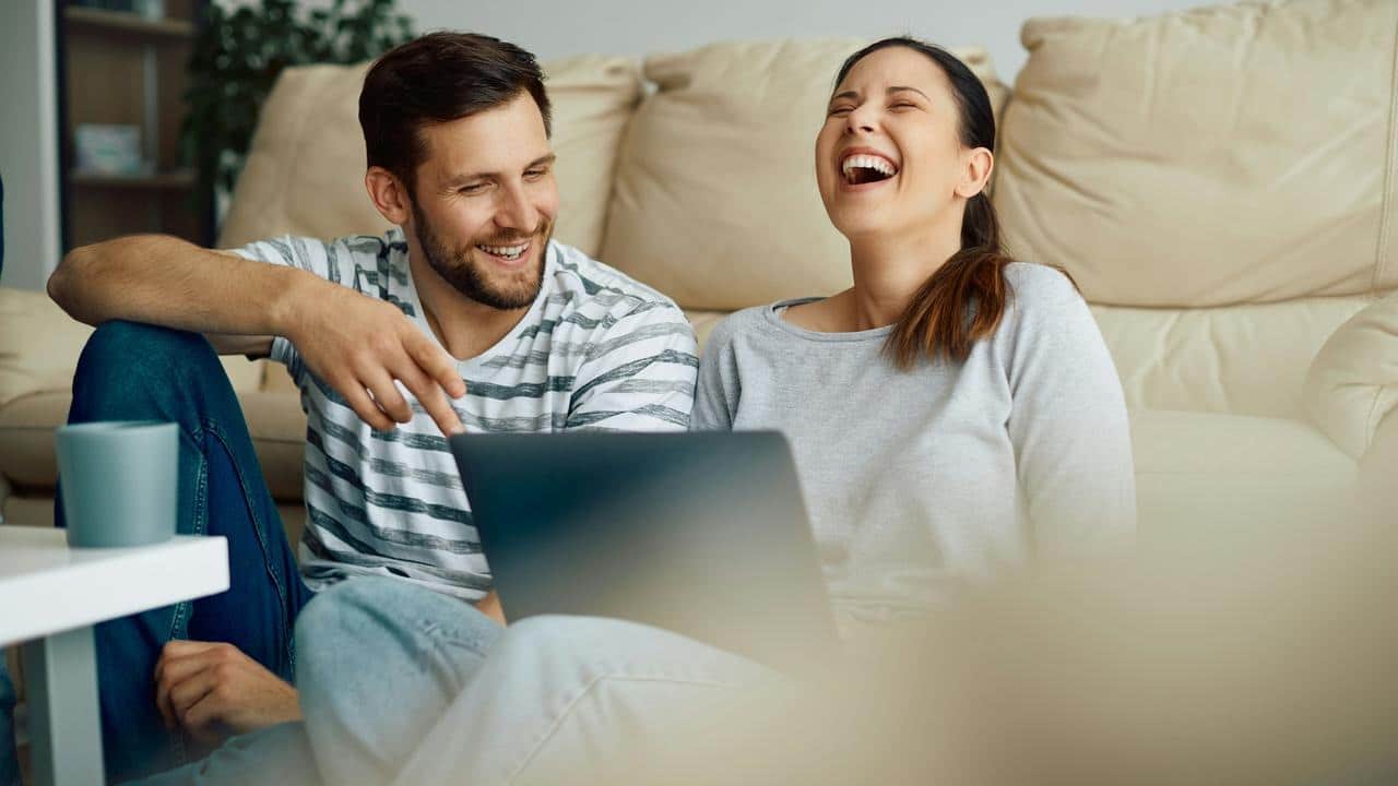 A couple laughing together while looking at a laptop.
