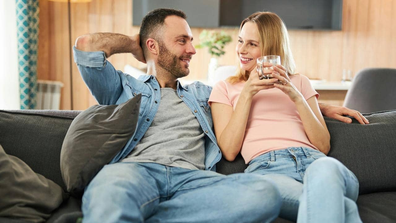 A couple lounging on a couch, smiling and sipping drinks.