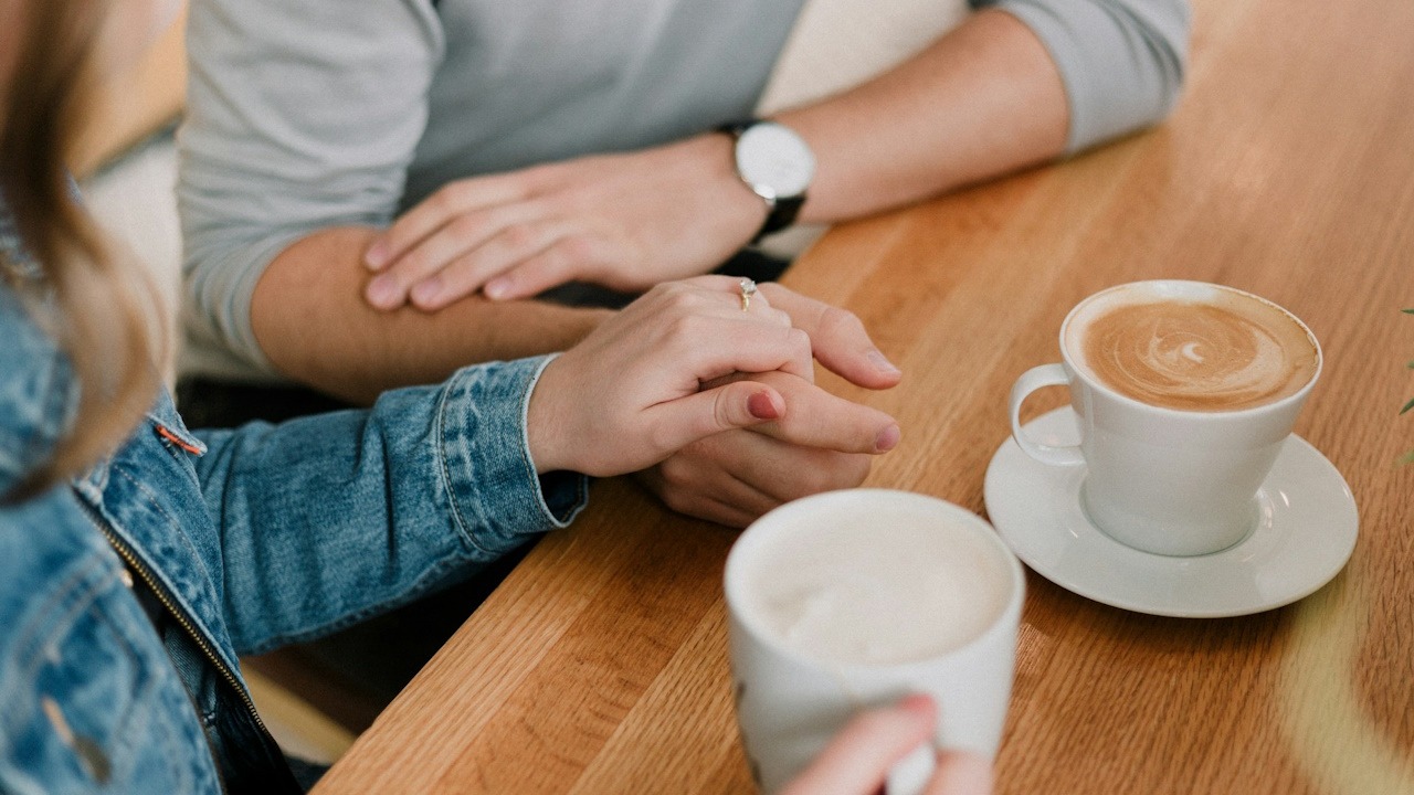 A couple holding hands while having coffee at a table and having a conversation.
