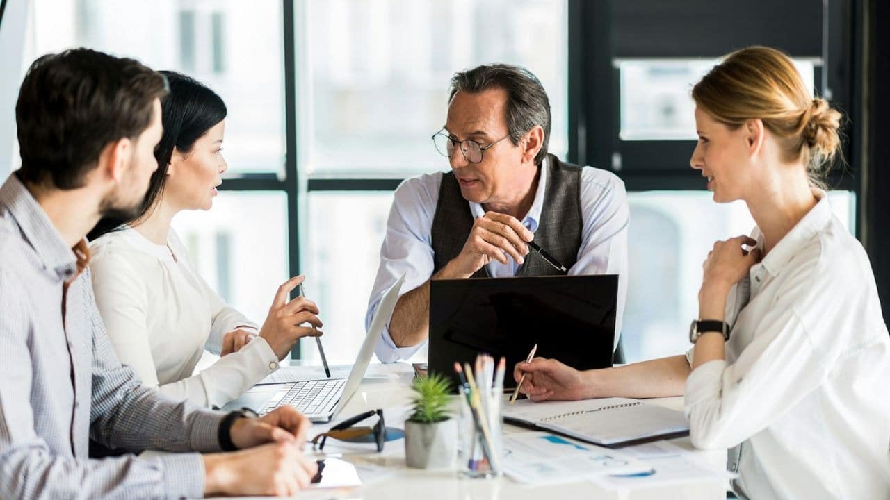 Four people, two men and two women, are engaged in a business discussion around a table.