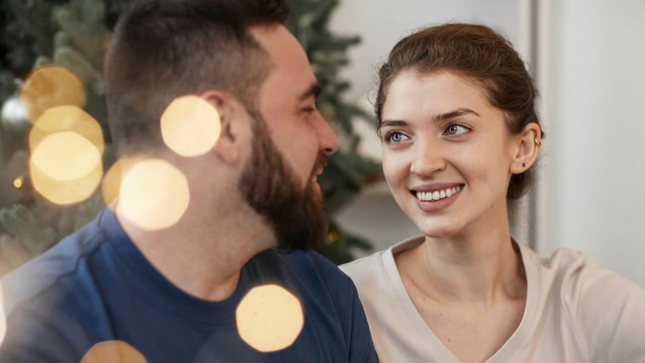 A happy man and woman are smiling at each other, with blurred lights in the foreground.