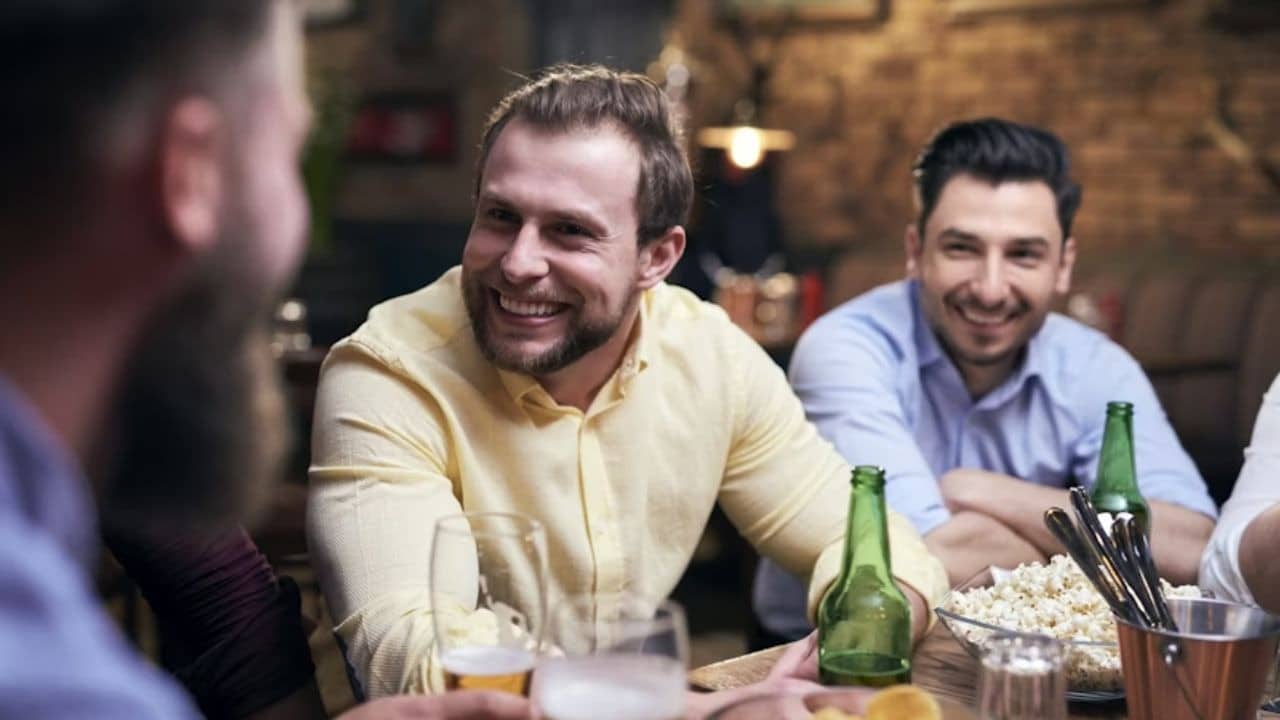 Man laughing with friends at a casual dinner enjoying food and drinks