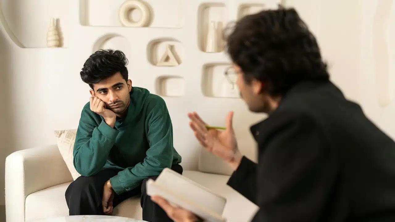 Two men sitting on a couch talking to each other.