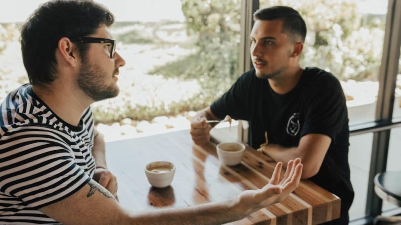 A man talking while his friend listens carefully over coffee