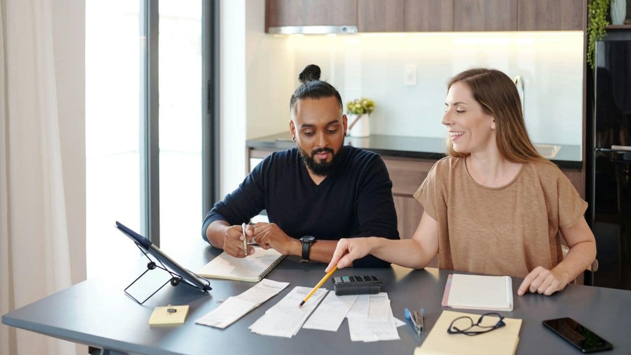 A smiling woman points to a receipt while a man with a man bun looks at it.