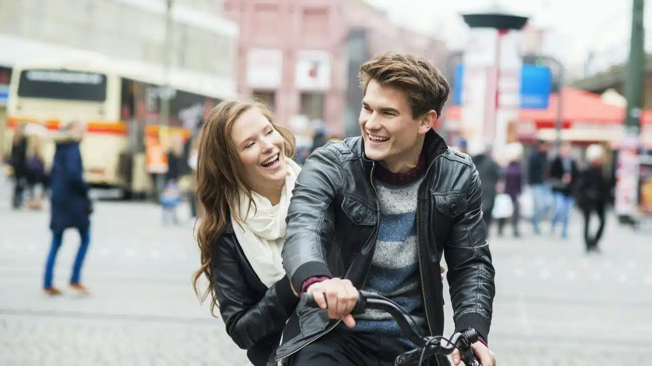 A smiling couple on a bike, riding together and laughing in a city street.