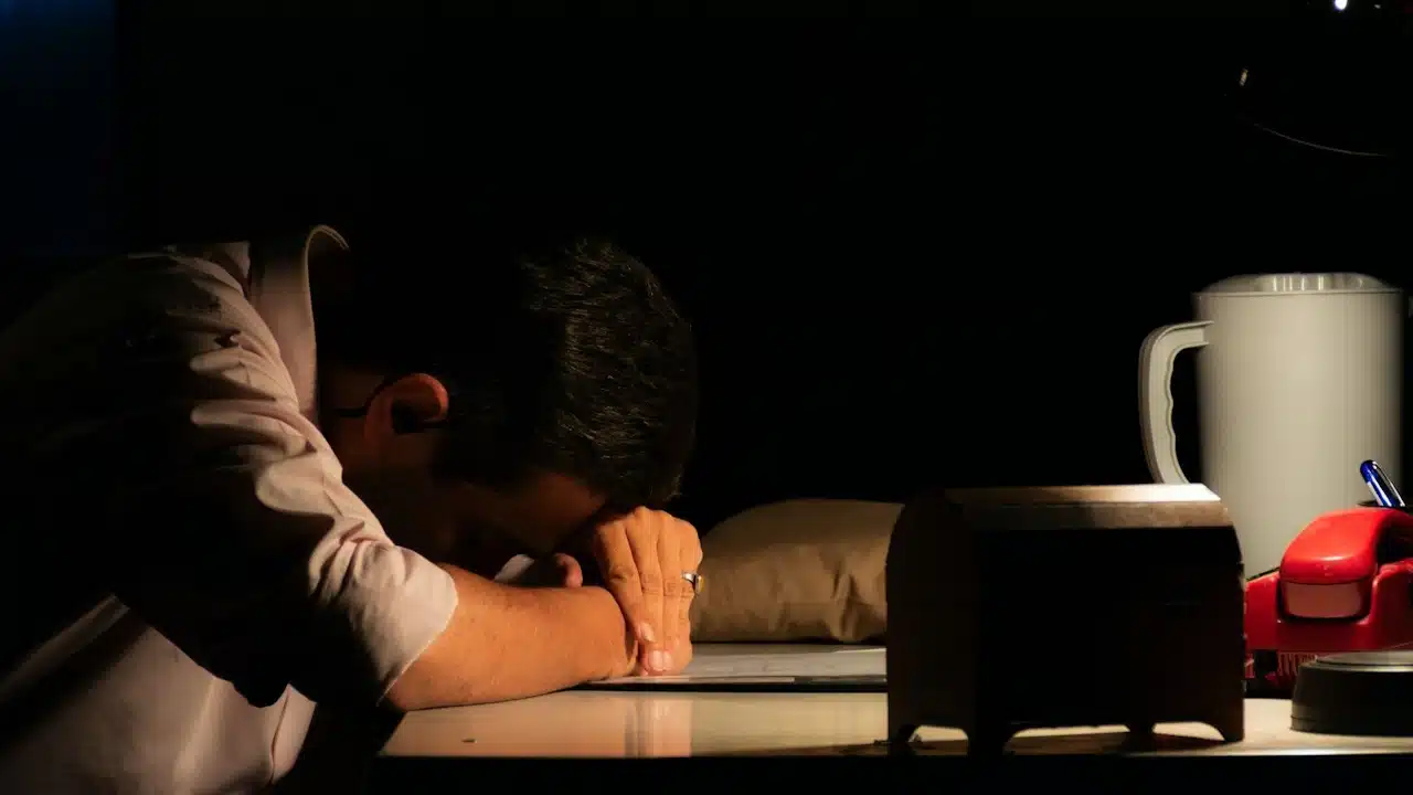 A close-up of a tired man with his head down on a desk.