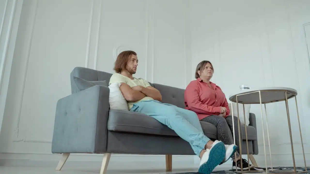 A man and woman sit apart on a couch, looking in opposite directions.