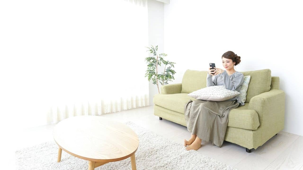 A man is holding a phone in his hands while sitting on a couch and looking at it.