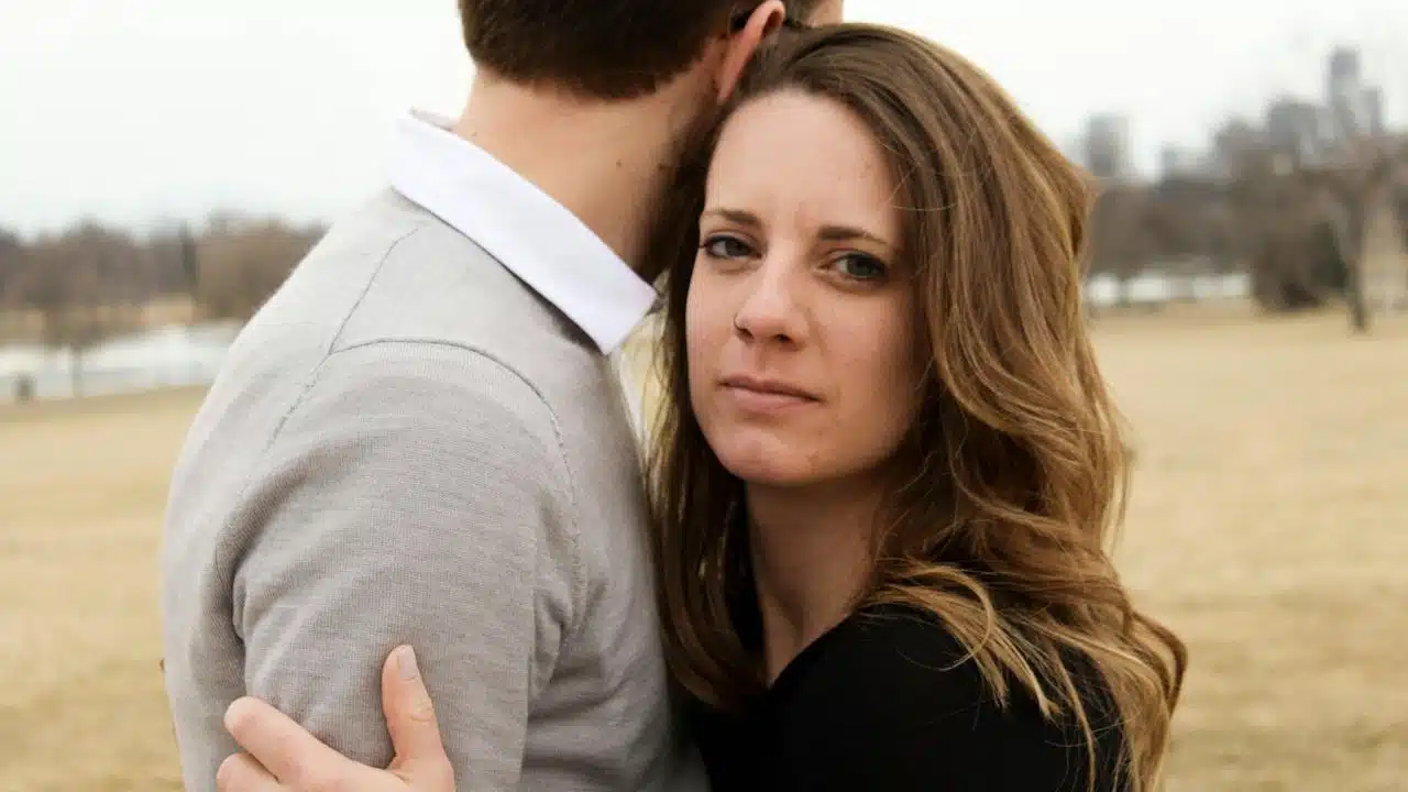 A woman hugging a man with a concerned expression on her face as they stand outside.