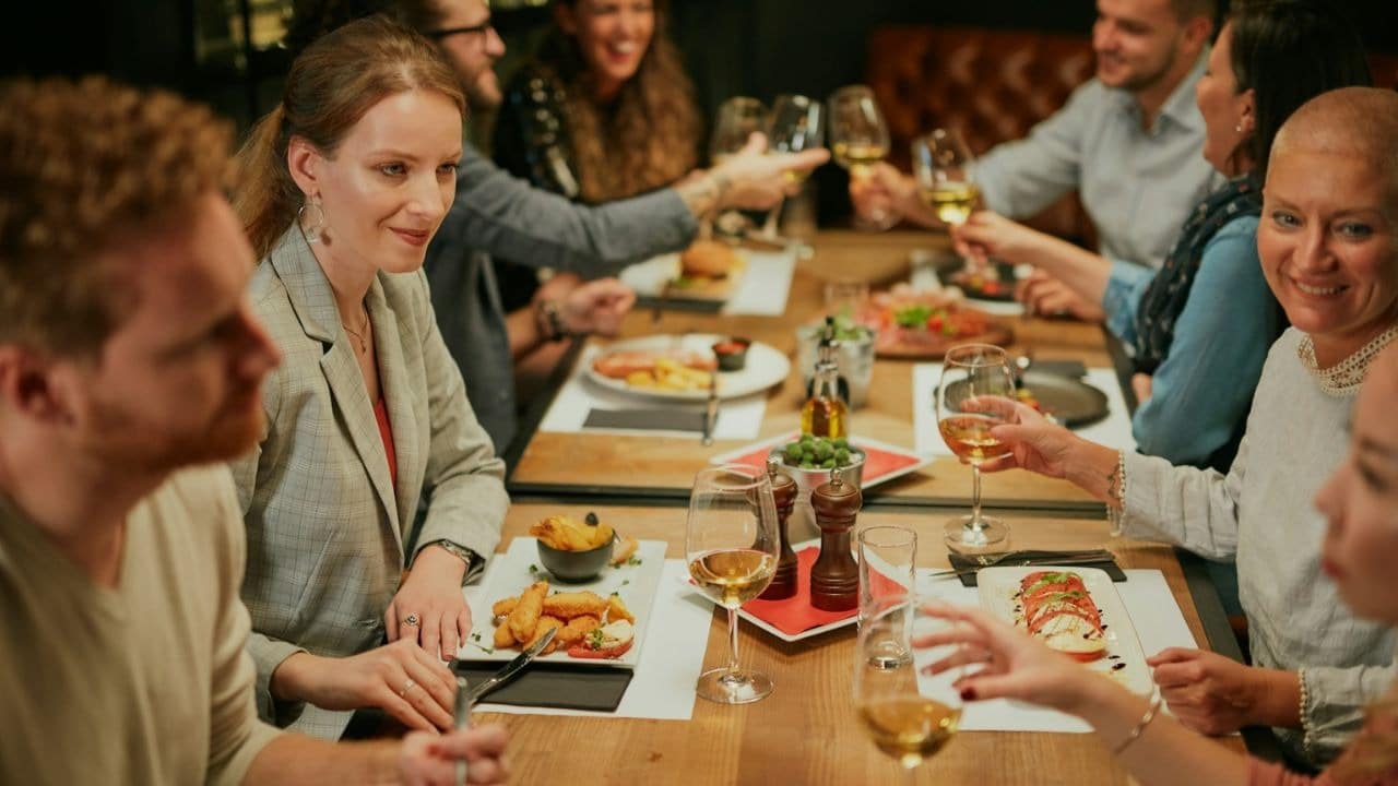 A group of people is seated around a table in a restaurant, enjoying their meal and drinks.